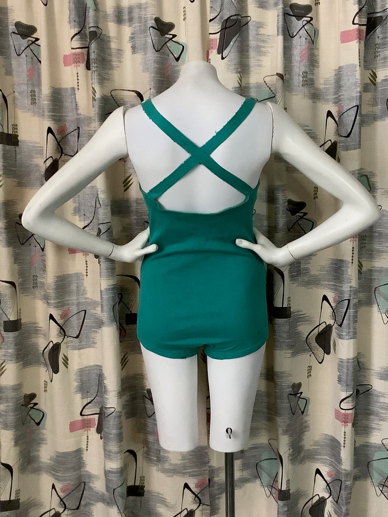 Pu&ograve; includere: Un costume da bagno blu turchese con un design a schiena incrociata. Il costume da bagno ha una scollatura rotonda e un taglio di gamba alto.