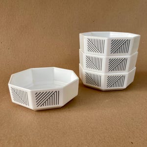 May include: Set of four white octagonal bowls with black geometric patterns. The bowls are stacked on top of each other.