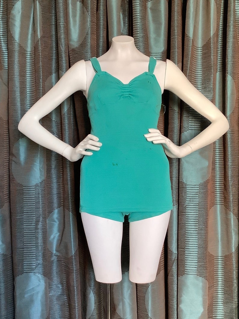 Pu&ograve; includere: Un costume da bagno intero color turchese con scollatura a cuore e spalline sottili. Il costume da bagno ha un dettaglio drappeggiato sul seno e uno stile a gamba corta a vita alta.