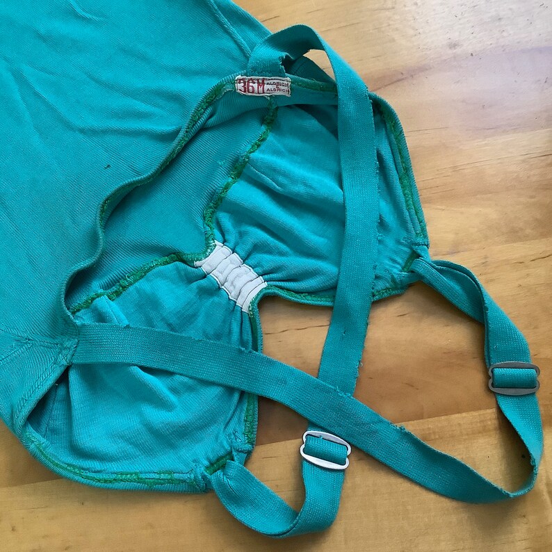 Pu&ograve; includere: Un top a spalline blu turchese con spalline regolabili e una fascia elastica bianca sul seno. L'etichetta sul top recita "36M".