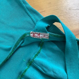 Pu&ograve; includere: Primo piano di una camicia blu turchese con una cucitura verde e un'etichetta bianca che recita "36M Aldrich".