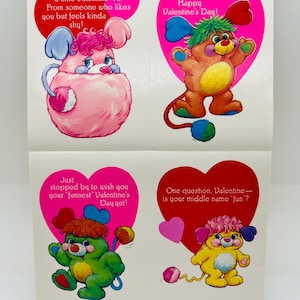 May include: Four vintage Valentine's Day cards featuring cartoon characters in various colors. Each card has a heart-shaped background with text. The characters are in pink, brown, green, and yellow, with curly hair and heart-shaped ears.