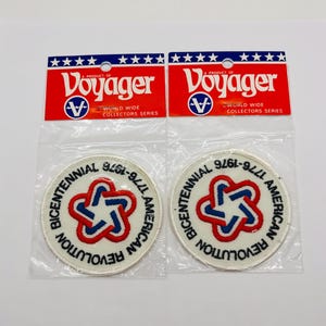 May include: Two circular embroidered patches in clear plastic packaging with Voyager brand headers. Each patch features a white background with a central red and blue star-like emblem and the text Bicentennial American Revolution 1776-1976.