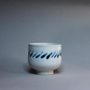 Puede incluir: Una taza de cerámica blanca con un asa negra y el texto "But First, Coffee" en negrita negra. La taza se encuentra sobre un fondo neutro, resaltando su diseño sencillo.