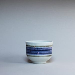 Puede incluir: Una taza de cerámica blanca con un asa negra y el texto "But First, Coffee" en negro, con una fuente de estilo manuscrito. La taza está sobre una superficie blanca.