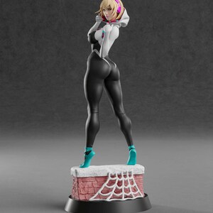Op de afbeelding: Een 3D-geprinte figuur van een vrouwelijke superheld in een zwart-wit pak, turquoise schoenen en een witte hoodie. De figuur staat op een baksteenachtige basis met een wit spinnenwebontwerp. De figuur heeft blond haar en draagt een roze koptelefoon. De basis heeft de tekst "ABE3D" en "www.patreon.com/abe3d".