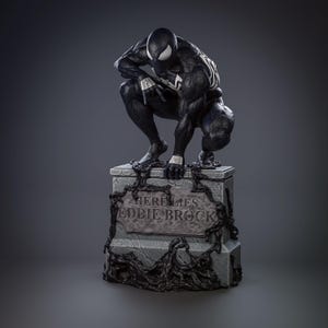 May include: A black and white statue of Venom crouching on a tombstone. The tombstone reads "Here Lies Eddie Brock" and is decorated with dark, organic tendrils. The statue has white accents and a menacing expression.