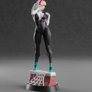 Op de afbeelding: 3D-geprinte beeldje van een vrouwelijke superheldin in een zwart-wit bodysuit, staand op een bakstenen structuur. Ze heeft blond haar, een roze haarband en turquoise hakken. De basis heeft de tekst "ABE3D" en een websiteadres.