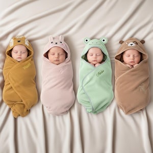 May include: Four swaddled babies in hooded towels. The towels are in shades of yellow, pink, green, and brown, each with an animal face design: lion, bunny, frog, and bear. Each towel is embroidered with a name.