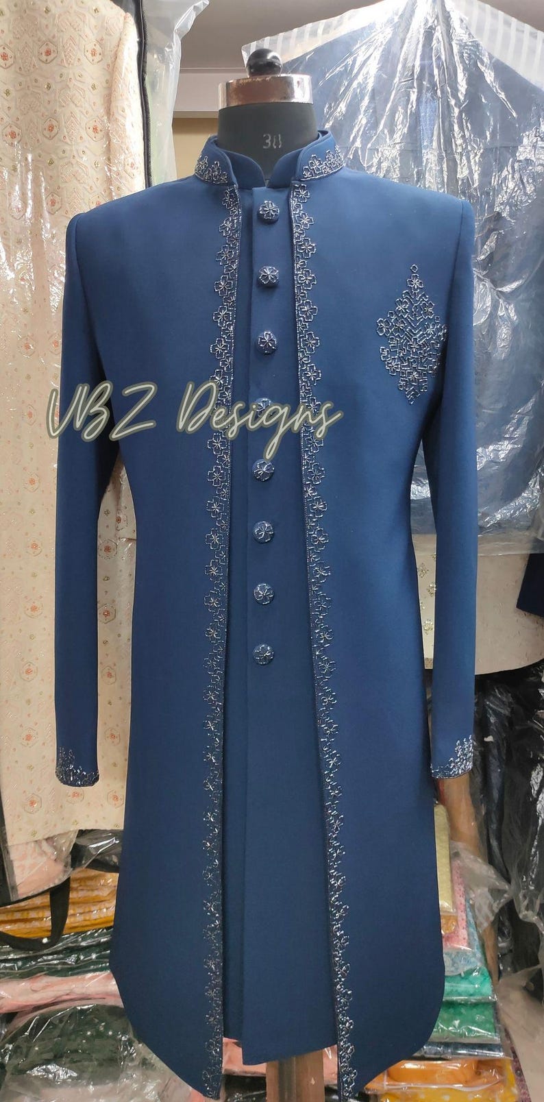 Puede incluir: Una larga chaqueta formal azul marino con intrincados bordados plateados en los bordes, el cuello y los pu&ntilde;os. La chaqueta presenta una fila de botones a juego y un dise&ntilde;o decorativo en el pecho. El texto "VBZ Designs" es visible.