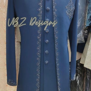 Puede incluir: Una chaqueta formal larga de color azul marino con intrincados bordados plateados en los bordes y en el pecho. La chaqueta tiene cuello mandar&iacute;n y botones decorativos. El texto "VBZ Designs" es visible.