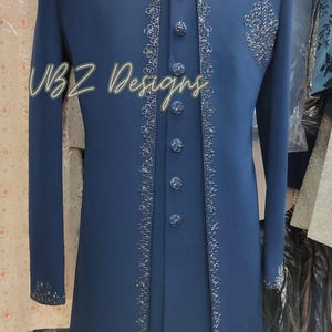 Puede incluir: Abrigo largo azul marino con bordados plateados en los bordes, cuello y pu&ntilde;os. Cuenta con botones a juego y un dise&ntilde;o bordado en el pecho. El texto "VBZ Designs" es visible. Prenda formal.