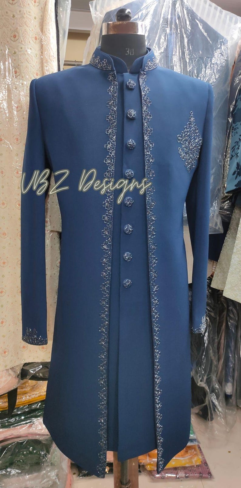 Puede incluir: Abrigo largo azul marino con bordados plateados en los bordes, cuello y pu&ntilde;os. Cuenta con botones a juego y un dise&ntilde;o bordado en el pecho. El texto "VBZ Designs" es visible. Prenda formal.