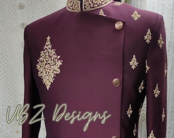 Puede incluir: Chaqueta formal burdeos con bordados dorados y cuello mandarín. La chaqueta presenta botones dorados y patrones florales decorativos. El texto "VBZ Designs" está escrito en cursiva en la parte inferior de la chaqueta.
