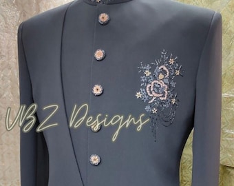 Puede incluir: Chaqueta de traje gris carbón con bordados florales y botones decorativos. La chaqueta presenta un cuello mandarín con detalles bordados y el texto "VBZ Designs" en cursiva.