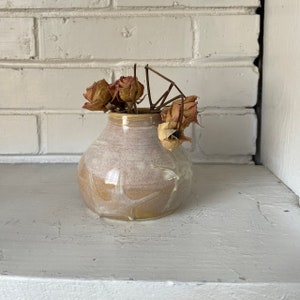 May include: A small, white and brown ceramic vase with a round body and a wide opening. The vase is filled with dried roses.