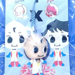 Könnte beinhalten: Ein Kewpie Honey Schlüsselanhänger mit einer zentralen Kewpie-Puppe mit blauen, roten und weißen Akzenten, umgeben von Cartoon-Illustrationen. Der Anhänger enthält japanischen Text und das Kewpie Honey Logo.