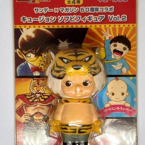 May include: A yellow and black tiger-themed soft vinyl figure of a character with a tiger head. The figure is wearing a yellow and black striped costume and black boots. The figure is packaged on a card with the text "サンデー×マガジン 50周年コラボ キュージョン ソフビフィギュア Vol.2" in Japanese.