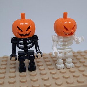 May include: Two Halloween skeleton figures with pumpkin heads. One skeleton is black and the other is white. Both figures have orange pumpkin heads with carved faces.