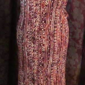 May include: A long, sleeveless dress with a red, white, and orange geometric pattern. The dress has a scoop neck and a fitted bodice.