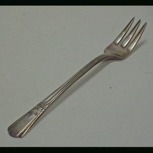 May include: A silver fork with a decorative handle. The fork has four tines and a long, slender handle.