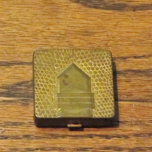 May include: A gold-colored metal compact with a textured, embossed design. The compact has a hinged lid and a small, rectangular mirror inside.