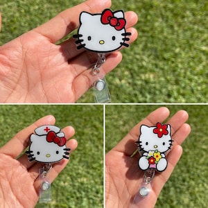 May include: Three Hello Kitty retractable badge holders. Each features a white cat face with black details and a red bow. One has a nurse's hat, another a flower, and the third a classic bow. The badge reels are attached to a clear plastic clip.