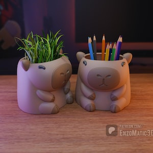 May include: Two beige capybara-shaped desk organizers. One holds green plants, the other colored pencils. The organizers have a cartoonish design with rounded features. The image is set on a wooden surface.