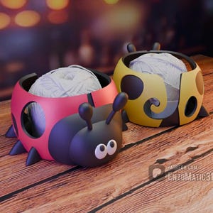 May include: Two ladybug-shaped yarn bowls. One is red and black, the other is yellow and black. Each bowl holds a ball of white yarn. The bowls have antennae and leg-like protrusions, sitting on a wooden surface.
