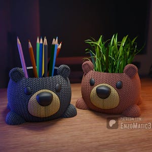 May include: Two bear-shaped desk organizers. One is dark blue and holds colored pencils. The other is brown and contains green plants. Both have a knitted texture and a tan snout.