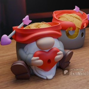 Puede incluir: Un bol de lana de gnomo rojo y blanco con una abertura en forma de corazón y una flecha en la parte superior. El gnomo sostiene un corazón rojo en sus manos.