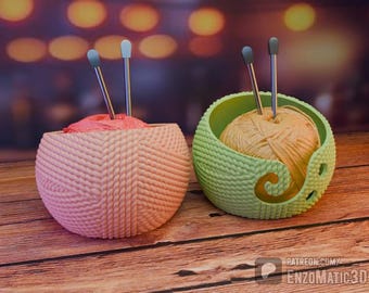 May include: Two yarn bowls, one pink and one green, sit on a wooden surface. Each bowl holds a ball of yarn and two knitting needles. The pink bowl has a textured, woven design, while the green bowl has a swirl cutout.