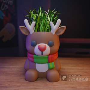 May include: A brown reindeer-shaped planter with white antlers, a red nose, and a green, red, and yellow scarf. The planter is filled with green grass. The planter is sitting on a wooden surface.