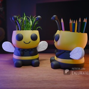 May include: Two yellow and black bee-shaped pencil holders. One is holding a bunch of coloured pencils and the other is holding a small potted plant. Both have white wings and black eyes.