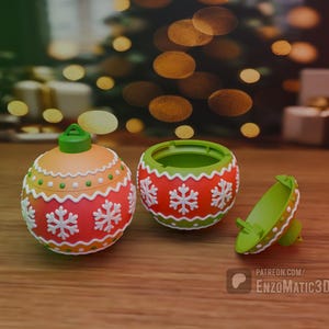 Puede incluir: Un adorno navideño rojo y verde con un diseño de copo de nieve blanco. El adorno está abierto y la mitad superior está separada de la mitad inferior.