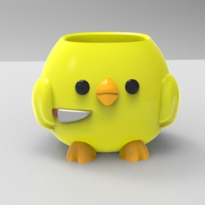 Puede incluir: Un macetero amarillo en forma de pollito con un cuchillo en su pico. El macetero tiene un cuerpo redondo y pequeñas patas.