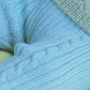 Puede incluir: Primer plano de un su&eacute;ter de punto azul claro con un patr&oacute;n texturizado. El su&eacute;ter est&aacute; doblado y las costuras son visibles.