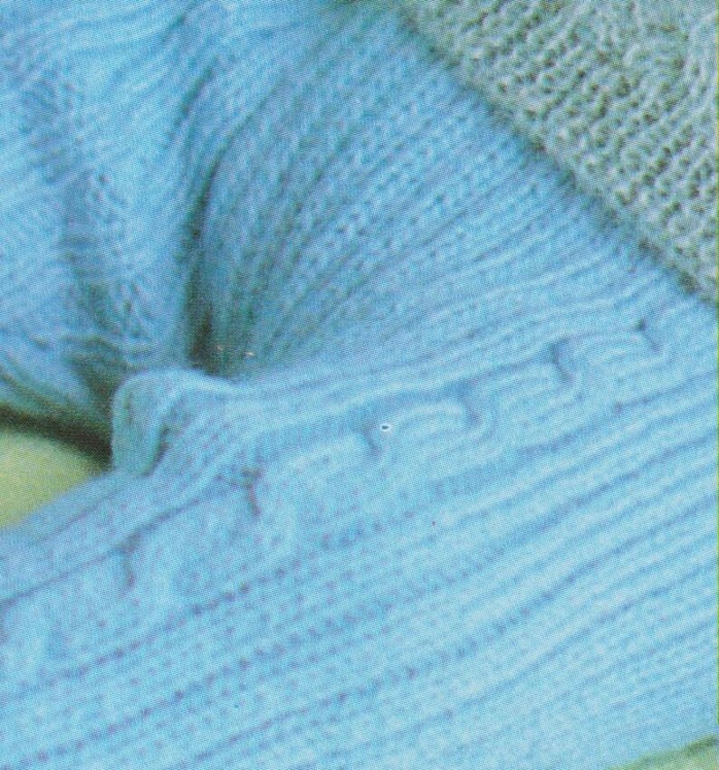 Puede incluir: Primer plano de un su&eacute;ter de punto azul claro con un patr&oacute;n texturizado. El su&eacute;ter est&aacute; doblado y las costuras son visibles.