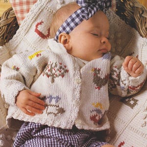 Könnte beinhalten: Ein weißer gestrickter Baby-Cardigan mit Knopfleiste und einem bunten Stickmuster aus Bäumen, Vögeln und anderen naturinspirierten Motiven. Der Cardigan wird von einem Baby mit einem schwarz-weiß karierten Stirnband getragen.