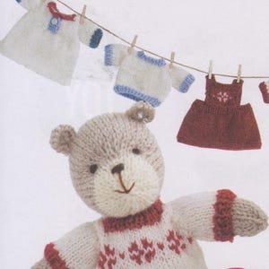 May include: A knitted teddy bear wearing a red and white sweater with a heart pattern. The bear is surrounded by miniature knitted clothing items hanging on a clothesline.
