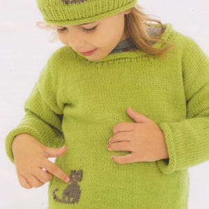 May include: A green knitted sweater with a brown cat design on the front. The sweater has a crew neck and long sleeves. A matching green knitted hat with a brown cat design is on the child's head.