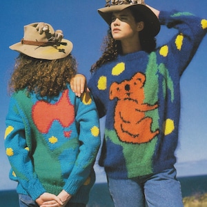 May include: Two women wearing blue and green sweaters with Australian animal designs. One sweater features a koala on a eucalyptus tree, the other features a red outline of Australia. Both women are wearing cowboy hats with stuffed toy koalas on top.