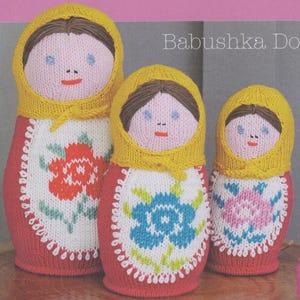 May include: Three knitted nesting dolls, or babushka dolls, with yellow hats and red, white and floral patterned dresses. The dolls are arranged in size order, with the largest doll at the front and the smallest doll at the back.