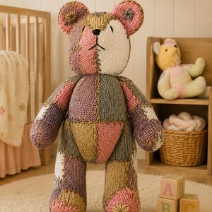 May include: A large, handmade patchwork teddy bear in soft pastel colors, including pink, lavender, and gold. The bear is knit with a variety of textures and patterns. Wooden ABC blocks are at the bear's feet. The bear is a nursery decor item.