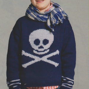 May include: A navy blue knitted sweater with a white skull and crossbones design. The sweater has white stripes on the cuffs and a white scarf around the neck.