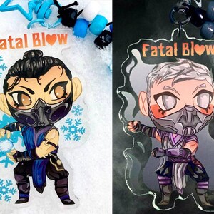May include: Two clear acrylic charms featuring a cartoon character with a blue and purple outfit, a black mask, and a heart symbol. The text "Fatal Blow" is printed on both charms.