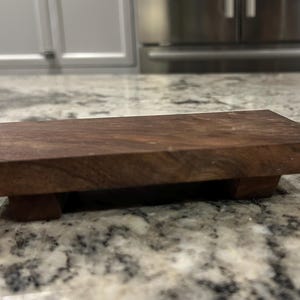 May include: A dark brown wooden serving tray with a rectangular shape and three legs. The tray is made of solid wood and has a natural finish.