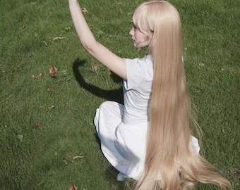 May include: A young person with long, blonde hair sits on a grassy field, wearing a white shirt and looking up at the sun.