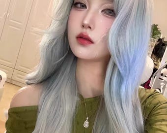 May include: A person with long, wavy, light blue hair and a green off-the-shoulder top. They are wearing a gold necklace with a small pendant. The person has fair skin, and is wearing makeup with pink lipstick.