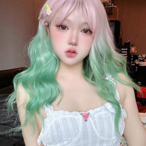 May include: A person with a pastel pink and green wig, styled with soft waves. They wear a white camisole with a small pink flower detail. A small green hair clip with a flower is visible.